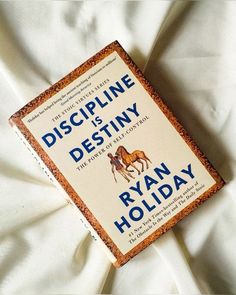 a book sitting on top of a white bed covered in sheets and pillows with the title, discipline is destiny by ryan holiday