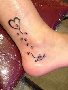 a person with a tattoo on their foot that says love and has paw prints in the shape of a heart