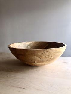 a wooden bowl sitting on top of a table next to a white wall in the background