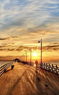 the sun is setting at the end of a pier with seagulls on it