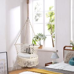 a bedroom with a bed, hanging chair and potted plant in the window sill