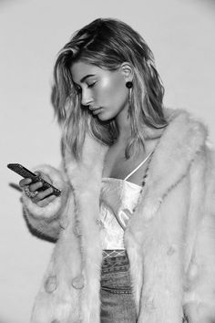 a black and white photo of a woman holding a cell phone while wearing a fur coat