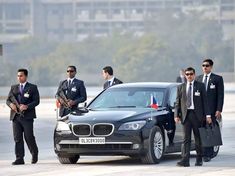 men in suits and ties standing next to a car with the hood open while another man is holding a briefcase