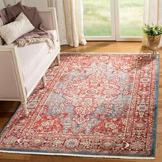 a red rug with blue border in front of a white couch and large open window