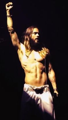 a man with long hair and no shirt on holding his hand up in the air