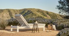 a white chaise lounge chair sitting on top of a gravel covered field next to mountains