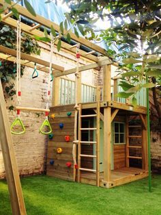 a wooden play structure with climbing bars and swings in the grass next to a brick wall