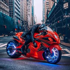 a man riding on the back of a red motorcycle down a street next to tall buildings