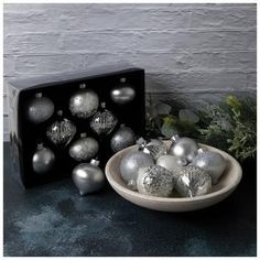 a bowl filled with silver and white ornaments next to a black box on a table