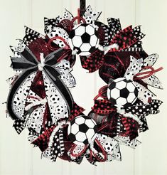 a soccer themed wreath hanging on a door with red, white and black ribbon around it