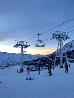 skiers and snowboarders at the bottom of a ski slope under a ski lift