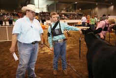 two men standing next to each other in front of a cow at a rodeo event