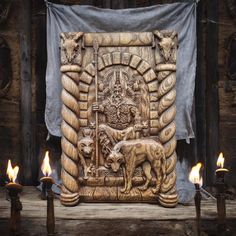 candles are lit in front of an intricately carved wall panel with animals on it