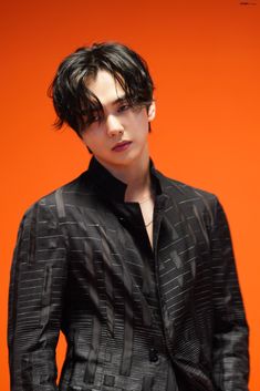 a young man with black hair wearing a suit and tie standing in front of an orange background