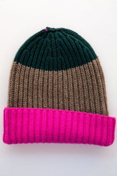 a knitted hat with pink and green stripes on the front, sitting on a white surface