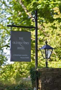 a sign hanging off the side of a building next to a lamp post and tree