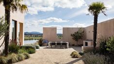 an outdoor dining area with palm trees and water in the back ground, surrounded by desert landscaping