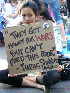 a woman sitting on the ground holding a sign that says they got money for wars but can't feed the poor