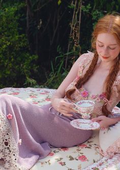 a woman sitting on the ground with a tea cup and saucer in her hands