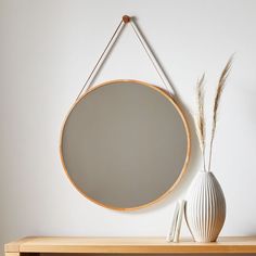 a white vase sitting on top of a wooden table next to a round mirror hanging from the wall