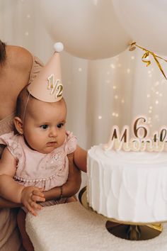 a woman holding a baby in front of a cake