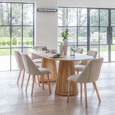 a dining room table with chairs and vases on it in front of large windows