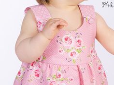 a baby girl wearing a pink dress with flowers on it's chest and smiling at the camera