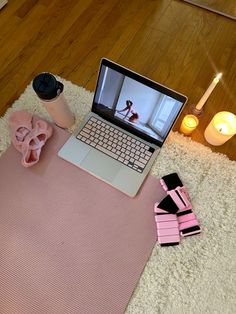 an open laptop computer sitting on top of a pink mat next to candles and other items