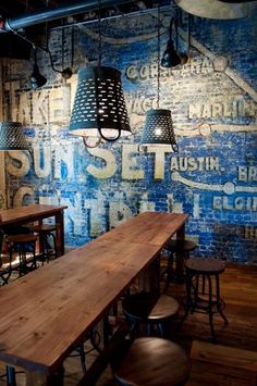 an industrial style restaurant with blue painted walls and wooden tables, stools and lamps