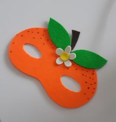 an orange mask with a flower on it is sitting on a white surface, ready to be used as a decoration