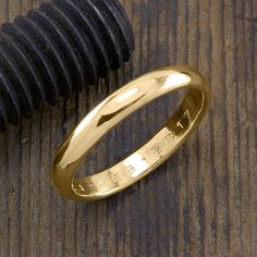 a gold wedding ring sitting on top of a wooden table next to a black object