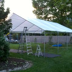 a large white tent set up in the grass with ladders and other equipment nearby