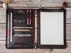 an open brown leather case with pens, pencils and other items inside on a wooden surface