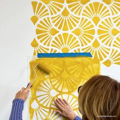 a woman is painting an art project on the wall with yellow paint and white stencils