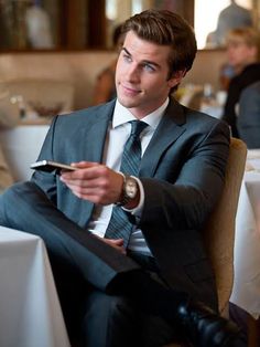 a man in a suit sitting at a table with his hand on the tie and looking off to the side