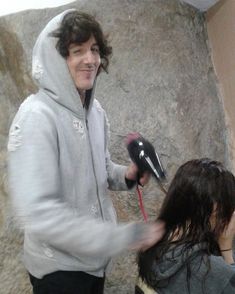 a man holding a hair dryer while standing next to a woman in front of a rock