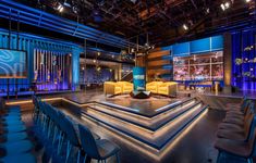 a room with chairs, couches and televisions on the walls is lit up by blue lights