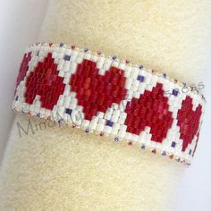 a red and white beaded bracelet on top of a white cloth covered wristband