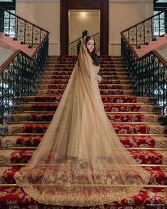 a woman in a wedding dress standing on the stairs with her veil draped over her head