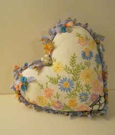 a heart shaped pillow with flowers on it sitting on a table next to a wall