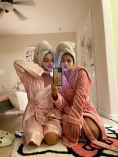 two women in robes are taking a selfie with their cell phone while sitting on the floor