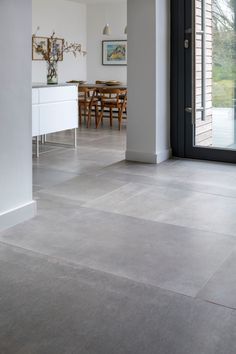 an open door leading to a dining room and kitchen area with white walls, flooring and furniture