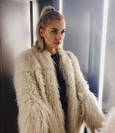 a woman standing in front of a mirror wearing a fur coat