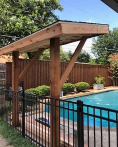 an outdoor swimming pool surrounded by black iron fence and wooden pavilion with pergolated roof