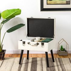 an open suitcase sitting on top of a wooden table next to a potted plant