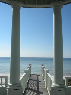 an empty walkway leading to the beach with columns on either side and water in the background