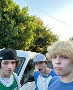 three young men standing next to each other in front of a white truck and trees