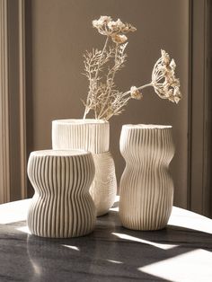 three white vases sitting on top of a table next to each other with flowers in them