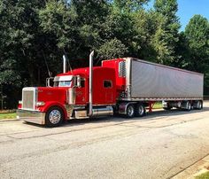 a red semi truck is parked on the side of the road in front of some trees