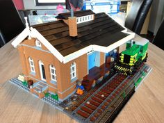 a lego train is on the tracks in front of a small house with a man standing next to it